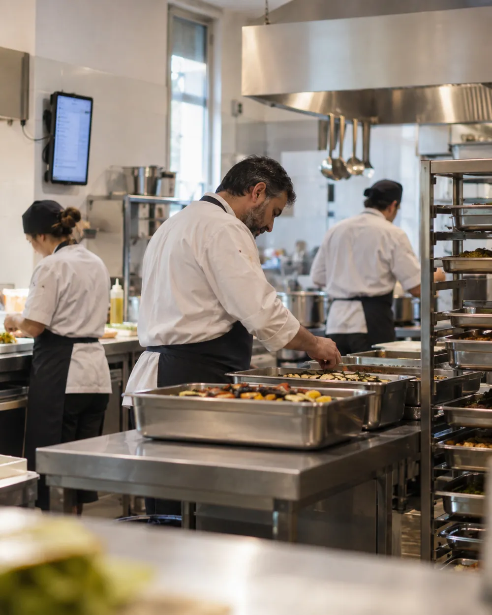 Chef in cucina di produzione con il tablet al muro e le teglie numerate